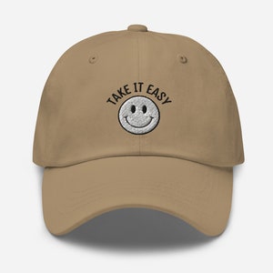 May include: A tan baseball cap with black embroidery that reads "TAKE IT EASY" and a white smiley face.