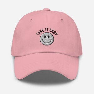 May include: Pink baseball cap with black embroidered text that says "Take It Easy" and a white smiley face.