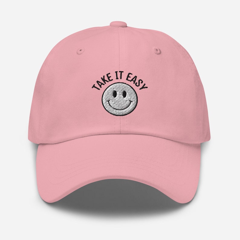 May include: Pink baseball cap with black embroidered text that says "Take It Easy" and a white smiley face.