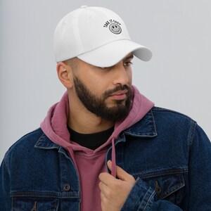 May include: A white baseball cap with black embroidery that reads "Take it Easy" with a smiley face. The cap is worn by a person with a beard.