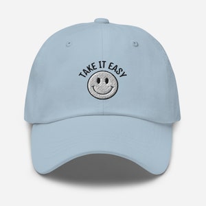 May include: A light blue baseball cap with black embroidery that reads "TAKE IT EASY" and a white smiley face.