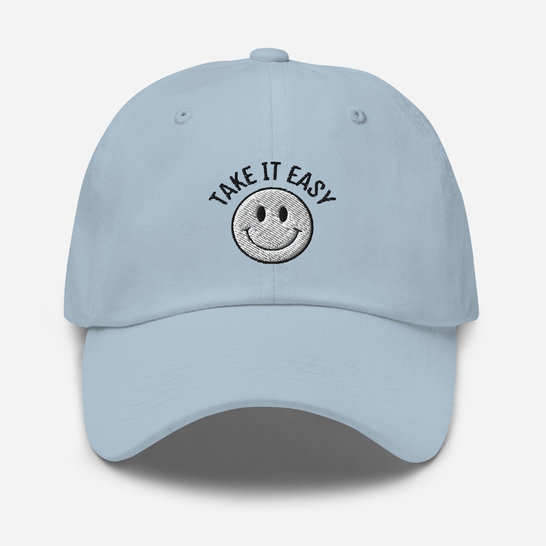 May include: A light blue baseball cap with black embroidery that reads "TAKE IT EASY" and a white smiley face.