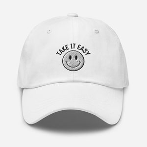 May include: White baseball cap with black embroidered text that reads "Take It Easy" and a smiley face.