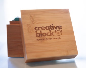 Op de afbeelding: Een houten doos met de woorden "creative block" en "open up. break through." gegraveerd op de bovenkant.