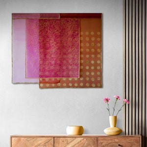 May include: A wooden cabinet with a geometric pattern on the doors and drawers. The cabinet is in front of a wall with a pink and gold abstract art piece hanging on it. There is a small yellow bowl on top of the cabinet.