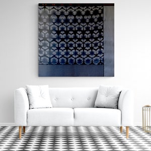 Puede incluir: Una pieza de arte mural cuadrada que presenta un patrón geométrico de estilo shibori en azul oscuro y blanco con un motivo repetitivo en forma de estrella, un panel vertical gris sólido a la derecha y una banda azul texturizada en el borde inferior.