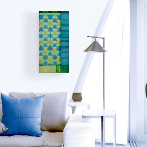 Puede incluir: Un sofá blanco con un cojín azul y una manta se encuentra en una sala de estar moderna. Una lámpara de pie con una pantalla plateada se encuentra junto a una pequeña mesa auxiliar blanca. Una pintura abstracta colorida cuelga de la pared.