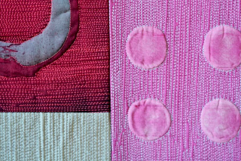 May include: A close-up of a pink fabric with white stitching, featuring three large pink circles. The fabric is textured and has a subtle sheen.