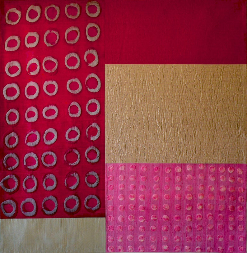 May include: Abstract art quilt with a red, gold, and pink color scheme. The quilt is made up of three sections, each with a different pattern. The left section features a repeating pattern of circles, the middle section has a textured gold fabric, and the right section has a repeating pattern of small pink circles.