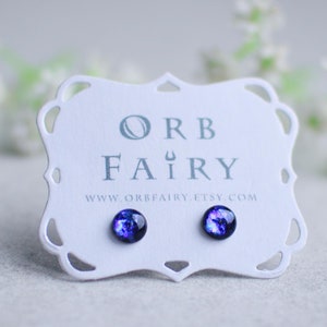 May include: A pair of small, round, blue and purple galaxy-themed stud earrings on a white card with the text "ORB FAIRY" and "www.orbfairy.etsy.com".