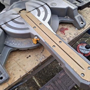 May include: A grey and black mitre saw with a wooden guide rail. The saw has a protractor with markings for 0, 15, 22.5, 30, 31.6, and 45 degrees.