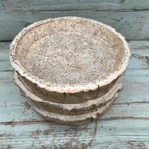 Może przedstawiać: Trzy stosy betonowych doniczek o szorstkiej, fakturowanej powierzchni. Doniczki są jasnobeżowe z lekko ciemniejszym, szarym, kropkowanym wzorem.