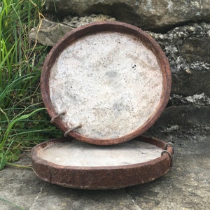 May include: Two round, rusty metal lids with a white, textured interior. The lids are stacked on top of each other.