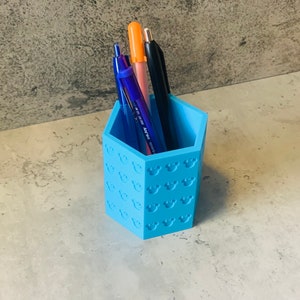 May include: A light blue pencil holder with a Mickey Mouse pattern. The holder is filled with pens and pencils.