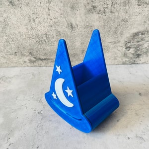 May include: A blue plastic pencil holder shaped like a wizard's hat with a white crescent moon and stars design.