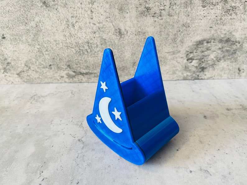 May include: A blue plastic pencil holder shaped like a wizard's hat with a white crescent moon and stars design.
