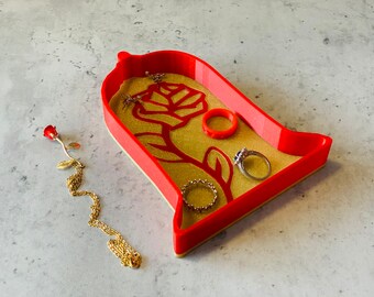 May include: Red and gold trinket dish shaped like a rose in a glass dome. The dish has a gold glitter finish and features a red rose design.