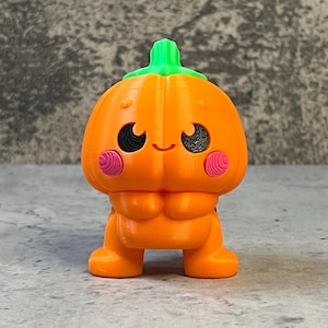 K&ouml;nnte beinhalten: Eine 3D-gedruckte orangefarbene K&uuml;rbisfigur mit gr&uuml;nem Stiel, schwarzen Augen und rosa Wangen. Der K&uuml;rbis hat ein l&auml;chelndes Gesicht und steht auf zwei orangefarbenen Beinen. Eine niedliche Halloween-Dekoration.