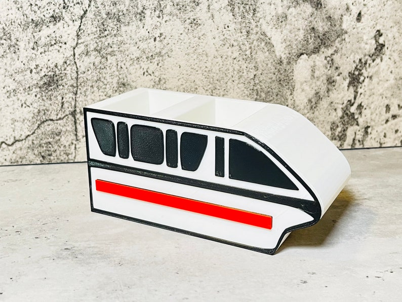 May include: White desk organizer shaped like a monorail train with black windows and a red stripe.
