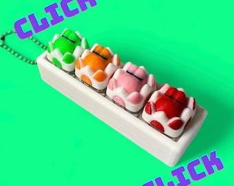 May include: A white rectangular tray holds four colorful, egg-shaped figurines. The eggs are green, orange, pink, and red, each with white and red accents. The word "CLICK" is displayed in purple text on the top and bottom of the image.