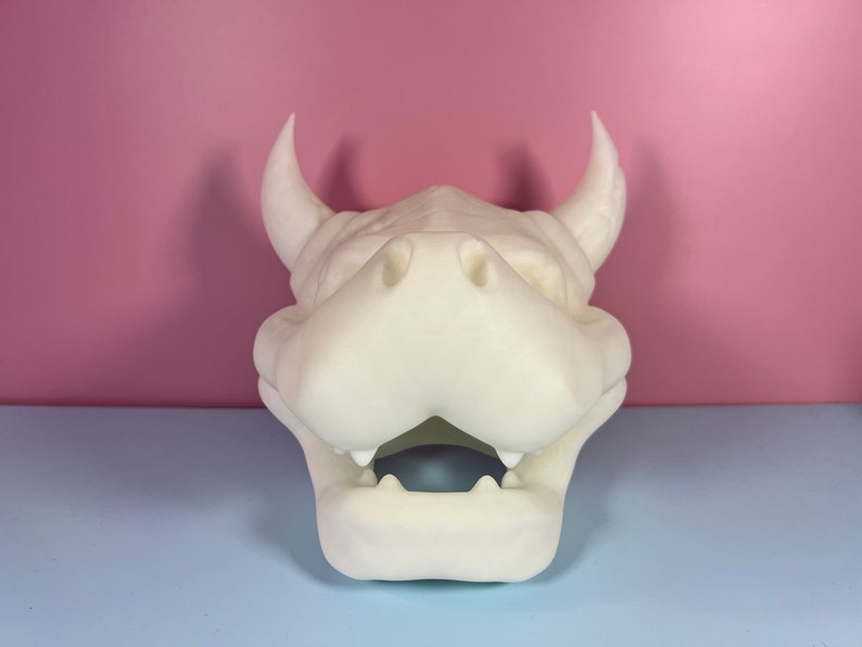Puede incluir: Cabeza de drag&oacute;n blanca impresa en 3D con la boca abierta y dientes afilados. La cabeza est&aacute; hecha de pl&aacute;stico blanco liso.