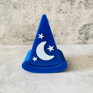 May include: A blue, 3D printed hat shaped like a wizard's hat with a white crescent moon and stars on the front.