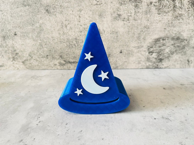 May include: A blue, 3D printed hat shaped like a wizard's hat with a white crescent moon and stars on the front.