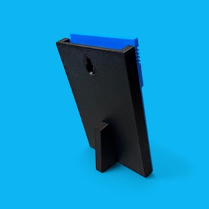 May include: A black picture frame with a blue insert, viewed from the back. The frame has a built-in stand and a keyhole for hanging. The frame is angled, showing the back and side profile against a blue background.