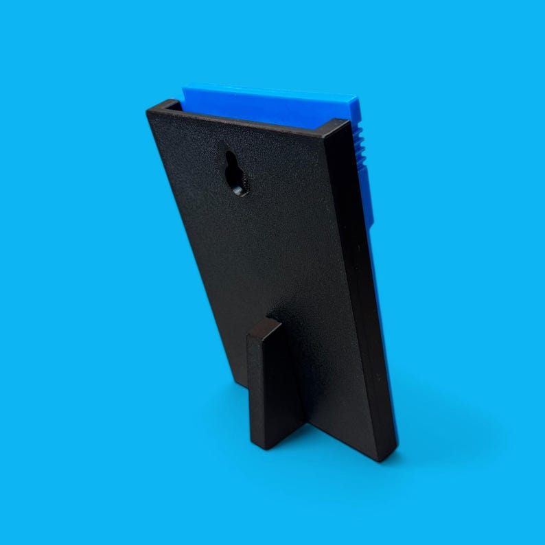 May include: A black picture frame with a blue insert, viewed from the back. The frame has a built-in stand and a keyhole for hanging. The frame is angled, showing the back and side profile against a blue background.