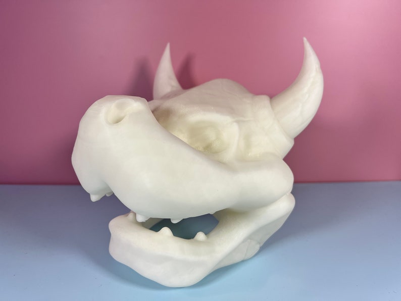 Puede incluir: Escultura de cabeza de drag&oacute;n impresa en 3D en blanco con cuernos y un hocico grande.
