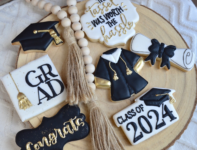 Pu&ograve; includere: Un set di biscotti di zucchero a tema laurea decorati con glassa nera e dorata. I biscotti raffigurano un cappello di laurea, un diploma, una toga, un cartello che dice "Grad", un cartello che dice "Classe del 2024" e un cartello che dice "Il fiocco &egrave; valso la pena".