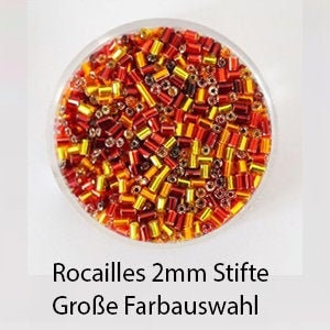 Könnte beinhalten: Nahaufnahme einer Auswahl kleiner, 2 mm großer Glasperlen in Rot-, Orange- und Goldtönen. Die Perlen befinden sich in einem durchsichtigen Behälter und sind mit "Rocailles 2mm Stifte Große Farbauswahl" beschriftet.