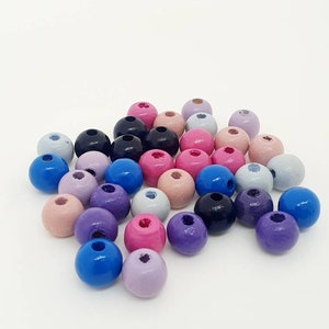 Könnte beinhalten: Eine Sammlung von Holzperlen in verschiedenen Farben, darunter Blau, Lila, Rosa und Grau. Die Perlen sind rund und haben ein Loch in der Mitte zum Auf fädeln.