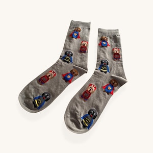May include: A pair of grey socks with embroidered superhero dog characters. The dogs are in various superhero costumes, including capes and masks. The socks are made of a soft, comfortable material.