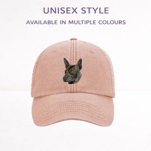 May include: A dusty pink baseball cap featuring an embroidered graphic of a dark-coloured dog head with pointed ears. The text UNISEX STYLE and AVAILABLE IN MULTIPLE COLOURS is printed above the cap in a simple, dark-coloured sans-serif font.