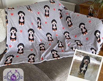 May include: A light gray throw blanket featuring a repeating pattern of cartoon Bernese Mountain Dog illustrations and small red hearts. The blanket is draped over a sofa, accompanied by a square photograph of a black and white dog in water.