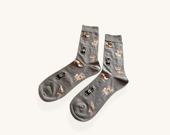 May include: A pair of grey crew-length socks featuring a repeating pattern of small, embroidered chihuahua dogs in various colors including tan, black, and white. The socks have a ribbed cuff at the top and a consistent knit texture throughout.