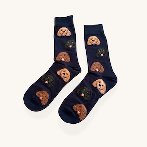 May include: A pair of navy blue crew socks featuring a repeating pattern of embroidered dog faces. The design includes small, detailed illustrations of curly-haired dogs in shades of tan, brown, and black, each with a pink tongue visible.