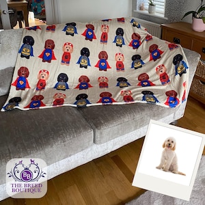 Könnte beinhalten: Eine cremefarbene Wohndecke mit einem sich wiederholenden Muster aus Zeichentrickhunden, die als Superhelden verkleidet sind, inklusive Umhängen und Masken. Die Hunde sind in Braun, Schwarz und Beige dargestellt und tragen rote, blaue oder gelbe Kostüme.