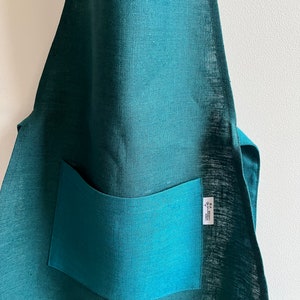 Może przedstawiać: Turkusowy fartuch lniany z dużą kieszenią i małą etykietą z napisem "Made with Love".