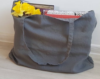 May include: A gray canvas tote bag with two handles, filled with books and yellow flowers. The bag is sitting on a light wood floor.