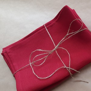 Peut inclure: Une pile de serviettes en lin rouge attachées ensemble avec de la ficelle. Les serviettes sont pliées en deux et la ficelle est enroulée autour du centre de la pile.