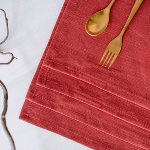 Könnte beinhalten: Ein Set aus drei goldfarbenen Besteckteilen, darunter eine Gabel und zwei Löffel, liegen auf einem roten Platzdeckchen. Das Platzdeckchen ist aus strukturiertem Stoff und hat einen dezenten Glanz.