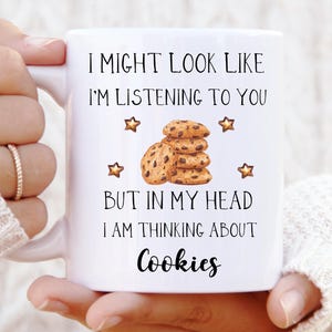 Könnte beinhalten: Weiße Keramiktasse mit dem Text "I MIGHT LOOK LIKE I'M LISTENING TO YOU BUT IN MY HEAD I AM THINKING ABOUT Cookies". Die Tasse zeigt einen Stapel Kekse und Sterne.