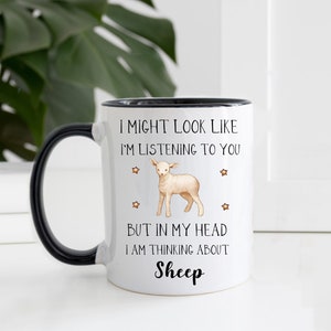 May include: White ceramic mug with a black handle. The mug has a black rim and features a black and white illustration of a lamb with the text "I might look like I'm listening to you but in my head I am thinking about Sheep."