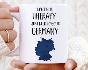 Puede incluir: Taza de cerámica blanca con texto negro que dice "No necesito terapia, solo necesito ir a Alemania" y una silueta azul de Alemania.