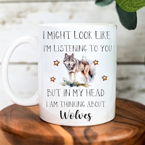 May include: White ceramic coffee mug featuring a wolf illustration and the text "I might look like I'm listening to you but in my head I am thinking about Wolves".