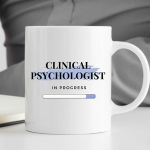 May include: White ceramic mug with a blue and white design. The mug says "Clinical Psychologist" with a progress bar that reads "In Progress".