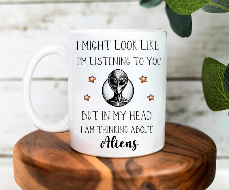 May include: White ceramic mug with a black and white illustration of an alien with the text "I might look like I'm listening to you but in my head I am thinking about Aliens".