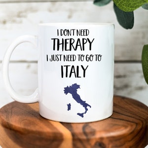 May include: White ceramic mug with a black graphic that reads "I don't need therapy I just need to go to Italy" with a blue outline of Italy.